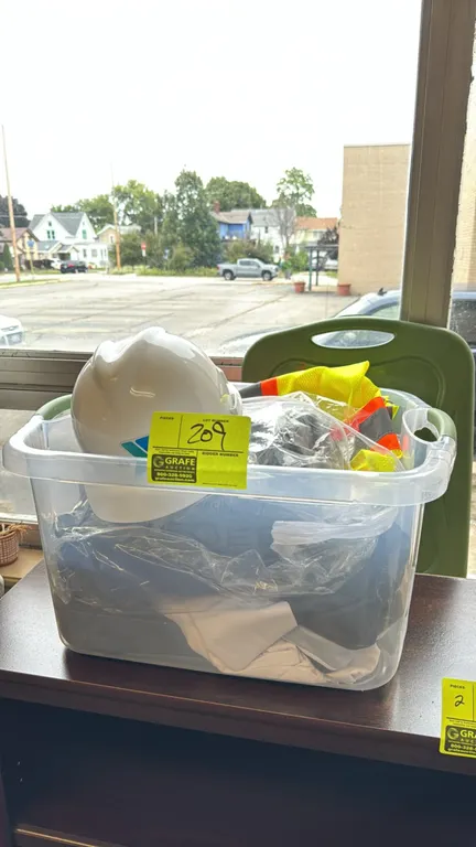 Assorted safety gear. Includes a white hard hat, high-visibility mesh safety vests with reflective striping, and other safety apparel. Housed in a cle