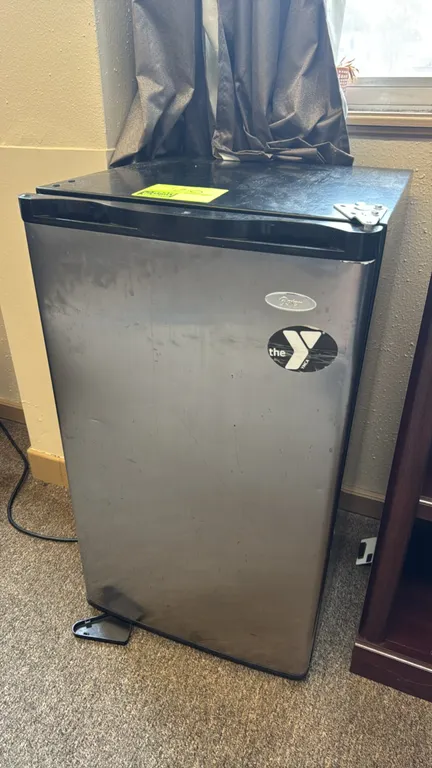Oster mini refrigerator. Features a stainless steel finish door, black cabinet, top freezer compartment with manual control dial, glass shelves, and d