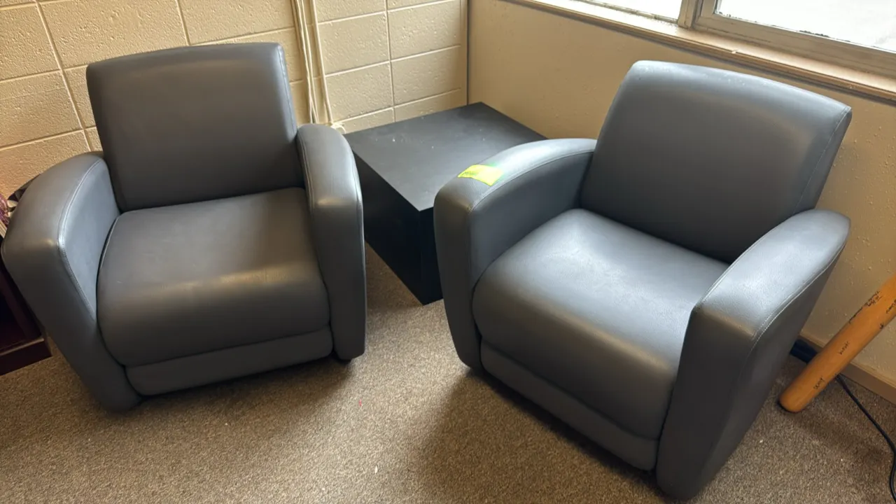 Faux leather padded armchairs with a side table. Features gray faux leather upholstery on the chairs and a black laminate block-style square side tabl