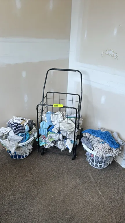 Bulk lot of assorted cleaning rags, towels, mop heads, and utility accessories. Includes various cotton rags, string mop heads, and a blue microfiber