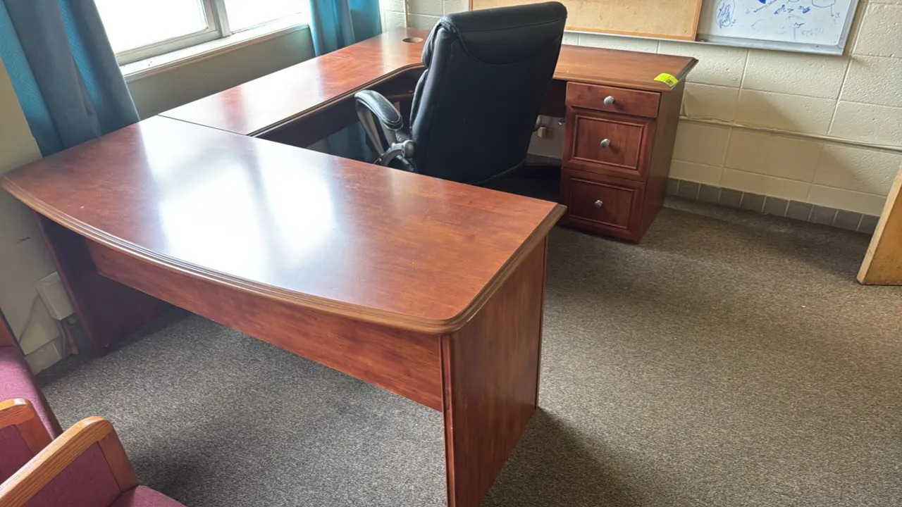 U-shape laminate desk suite in a cherry finish. Features a 3-drawer storage pedestal and a keyboard tray. Includes a high-back black vinyl office chai