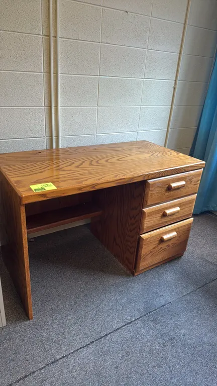 Wooden desk. Features a single-pedestal design with three right-hand drawers and an under-desktop open shelf. Oak-grain finish with matching wood draw