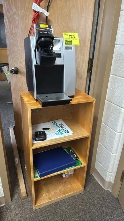 Keurig single-serve pod brewer with a small wooden bookcase. Brewer features a digital display, manual lever, and silver-tone finish. Bookcase feature