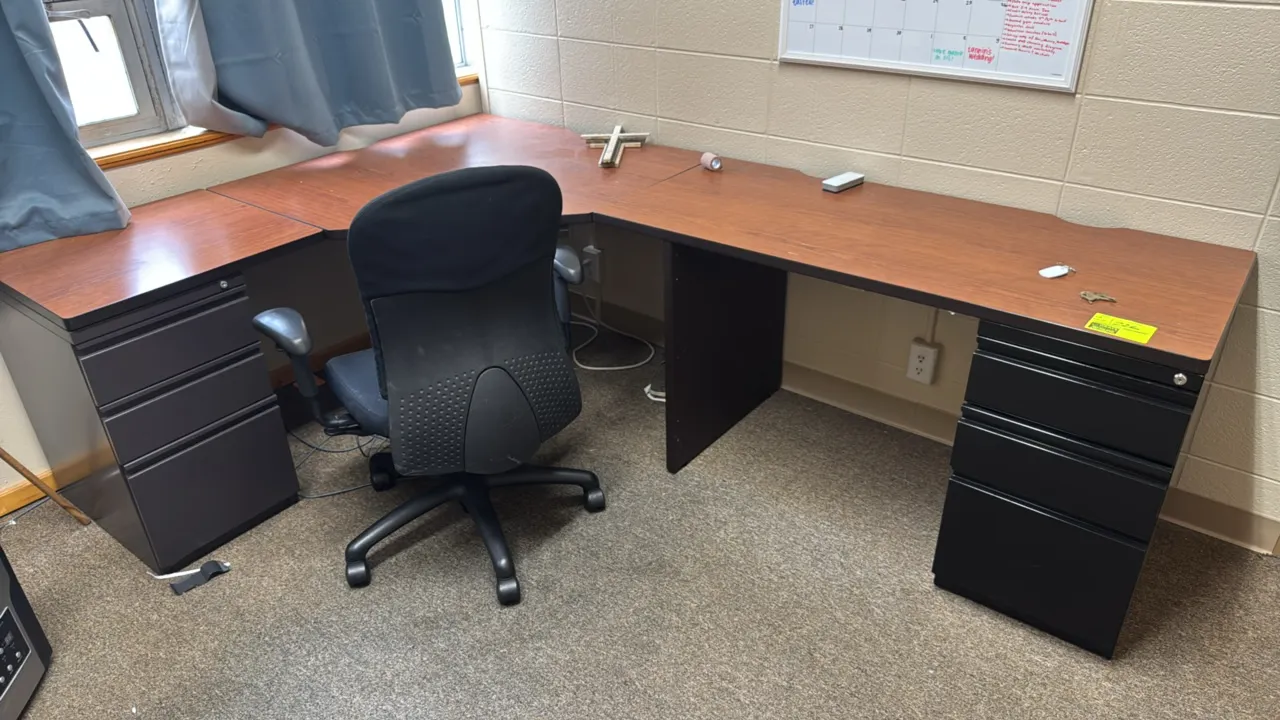 Metal and laminate corner desk with office chair. Desk features an L-shaped woodgrain laminate top, black metal framework, and two integrated 3-drawer