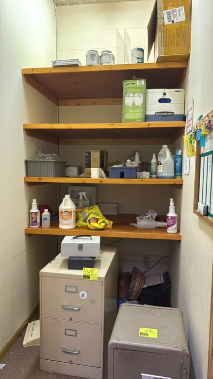 Remaining contents of a storage closet. Includes two metal cash boxes, blue cleaning rags, safety vest, Dynarex shoe covers, Crofton glass beverage di