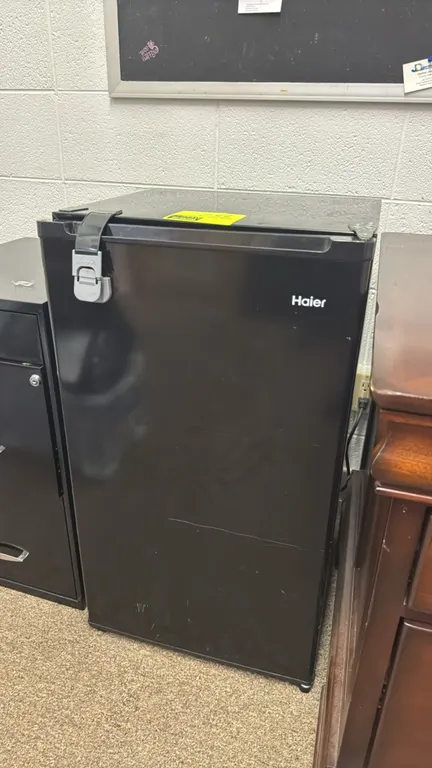 Haier mini refrigerator. Features a black finish, single-door design, two interior glass shelves, built-in door storage, and a top chiller compartment