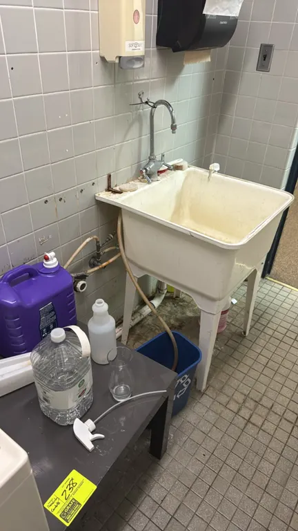 Remaining wash room contents. Includes a freestanding poly utility sink with faucet, a small grey laminate side table, assorted microfiber dust mop he
