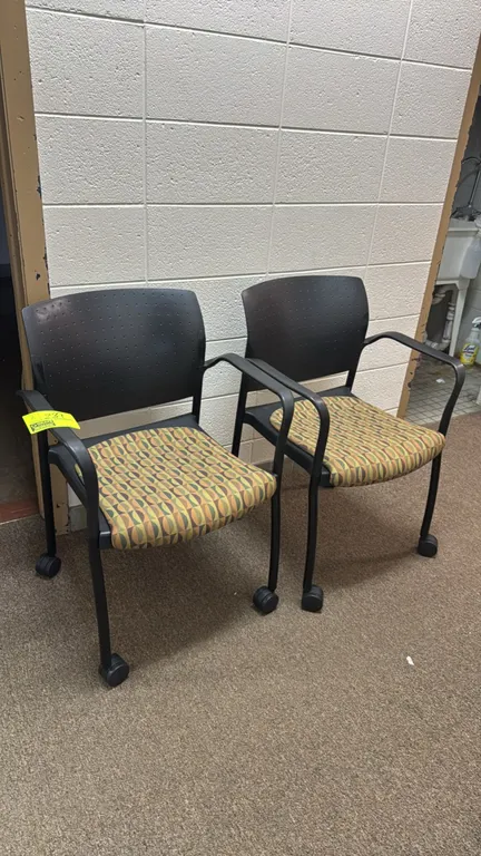 Portable office chairs. Features contoured black plastic backrests, patterned fabric padded seats, and integrated armrests. Mounted on black metal fra