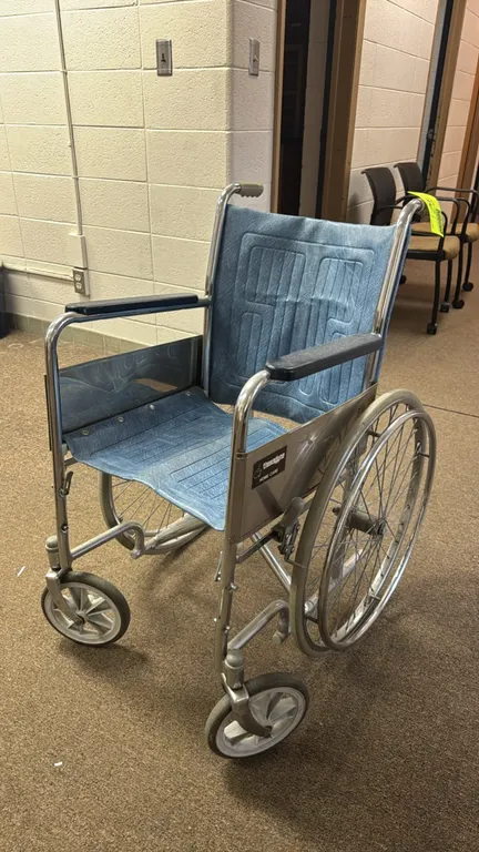 Theradyne manual wheelchair. Features a chrome-finished metal frame with blue textured vinyl seat and backrest upholstery. Equipped with padded armres
