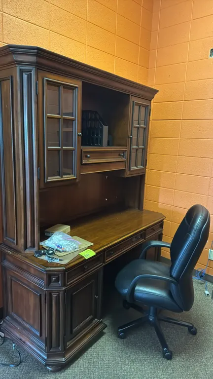 Wood desk suite. Includes 68"L double-pedestal wood desk with hutch, black high-back executive swivel chair, and oak-finished bookcase. Desk features
