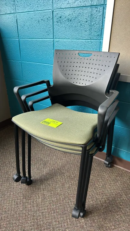 Padded stacking portable chairs. Features green fabric padded seats, perforated black poly backs with integrated handle grips, and armrests. Mounted o
