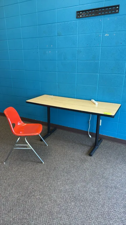Laminate table and chair set. Includes a 5'x2' table featuring a wood-grain laminate top and black metal T-base, paired with an orange molded plastic
