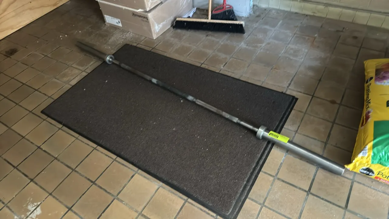 Men's Olympic barbell with floor mats. Features a knurled grip and rotating sleeves. 86"L. Includes two floor mats. Background items not included.