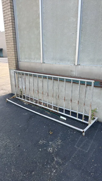 Metal bike rack. Features a grid-style frame with vertical rungs for bicycle parking. 8'L. Freestanding tubular metal base. Note: Item exhibits rust a