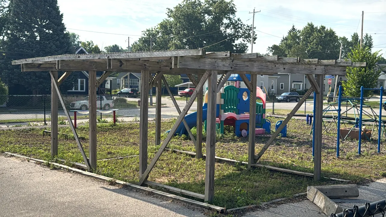 Wooden pergola. Freestanding outdoor structure features overhead rafters, crossbeams, and vertical posts with diagonal bracing. Weathered wood constru