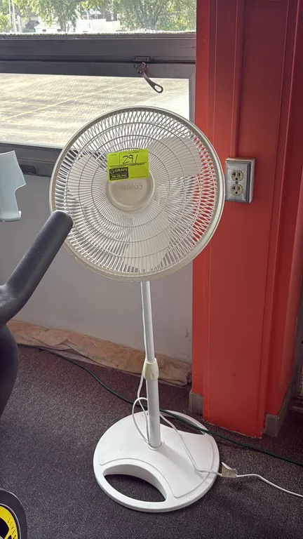 Lasko pedestal fan. Features white plastic construction, adjustable height, oscillating head, and multi-speed controls. Mounted on a circular base.