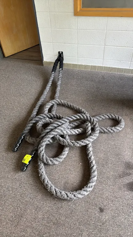 Synthetic battling exercise rope. Features a grey braided design with black heat-shrink grip handles on both ends. Designed for fitness, strength, and