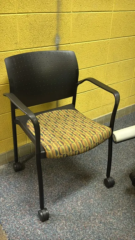 Rolling stackable padded chairs. Features patterned upholstered padded seats, perforated dark gray plastic backs, and integrated armrests. Stackable d