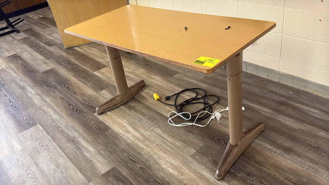 Laminate top desk. Features a woodgrain-style laminate top and a metal T-leg base. 48"L. Note: Base shows significant scuffing and finish wear.