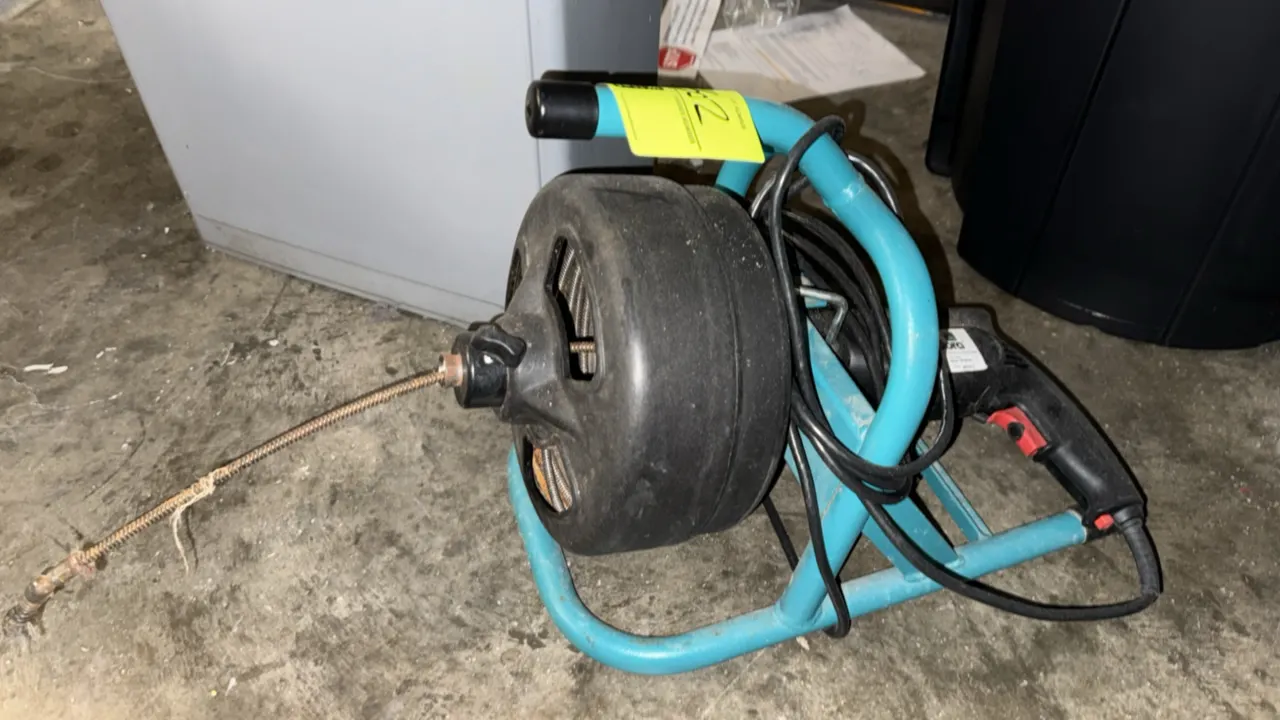 Cobra electric snake drain cleaner. Features a trigger-operated motor, integrated black drum with cable, and power cord. Mounted on a teal tubular met