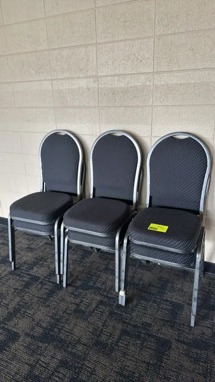 Metal upholstered padded chairs. Features textured dark fabric seat and backrest cushions with a crown-back design and integrated top handhold cutouts