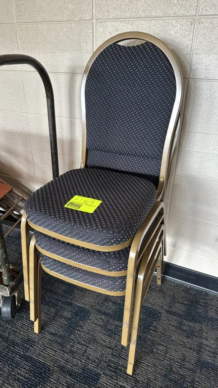 Metal upholstered banquet stack chairs. Features padded crown backrests and seats with dark patterned fabric upholstery. Gold-tone metallic frames. St