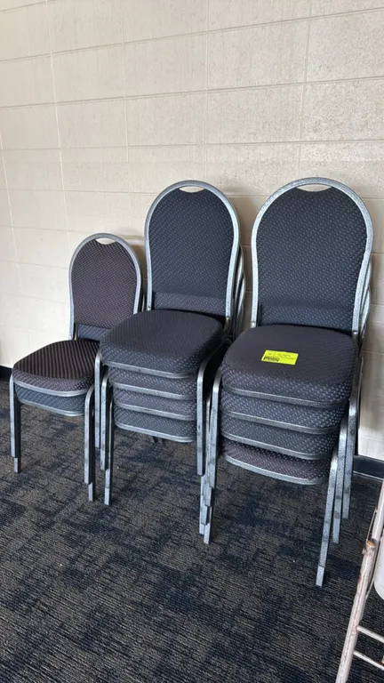 Padded metal banquet chairs. Features textured dark fabric upholstered seats and backrests. Silver-tone vein metal frames with top hand-holds. Stackab