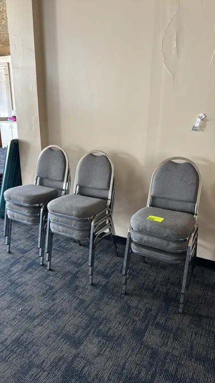 Metal upholstered padded stacking chairs. Features gray textured fabric padded seats and backs. Mounted on chrome-finished metal frames.