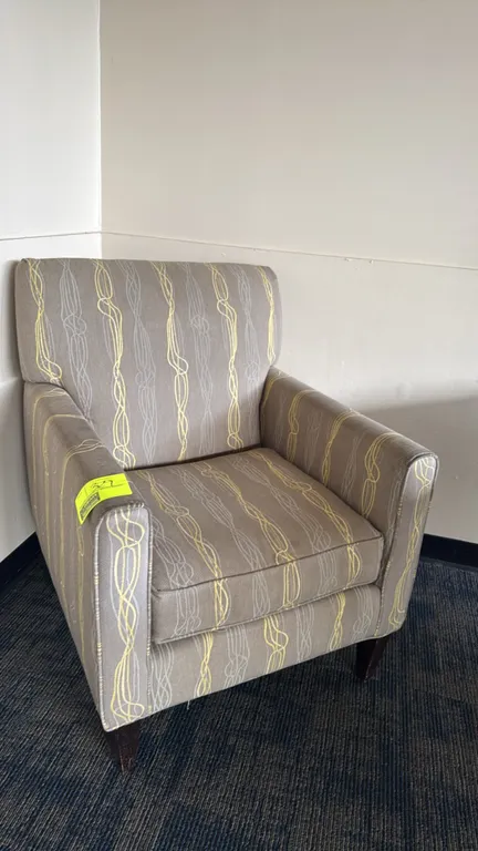 Upholstered padded lounge chair. Features taupe fabric upholstery with vertical yellow and white wavy line patterns, a padded backrest, and a loose se