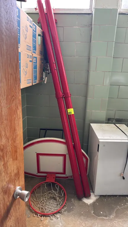 Multi-sport gymnasium standard posts and basketball backboard set. Includes two red-finished metal upright posts, with one post featuring a manual ten