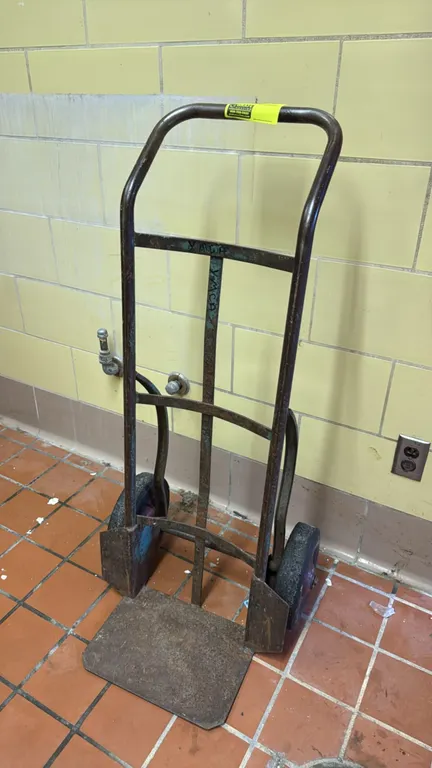 Metal 2-wheel hand truck dolly. Features a welded steel frame, curved vertical back straps, a flat steel nose plate, and two solid rubber wheels. Cent