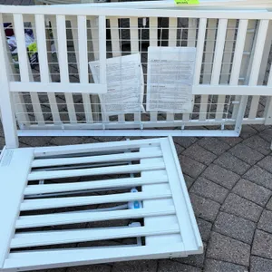 White children's crib and matching folding luggage rack. Crib features white-finished wood panels with a metal mesh mattress support. Included luggage