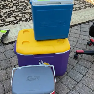 Assorted cooler lot. Includes (3) individual coolers: one blue Coleman Party Stacker cooler with a telescoping handle, one purple and yellow cooler wi
