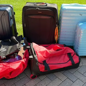 Assorted suitcases and travel bags. Includes hardside and softside wheeled suitcases in various sizes, a rolling red duffel bag, and folding travel to