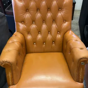 Executive office chair. Features brown button-tufted vinyl upholstery, padded roll arms with decorative detailed wood front trim, and a high-back desi