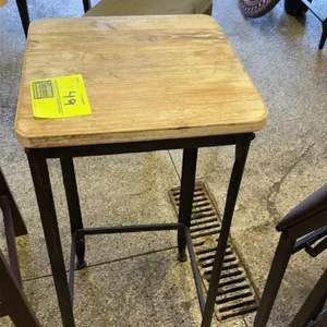 Plant stand featuring a square wood top with a light natural finish. Mounted on a dark-finished aluminum frame with lower stretchers.