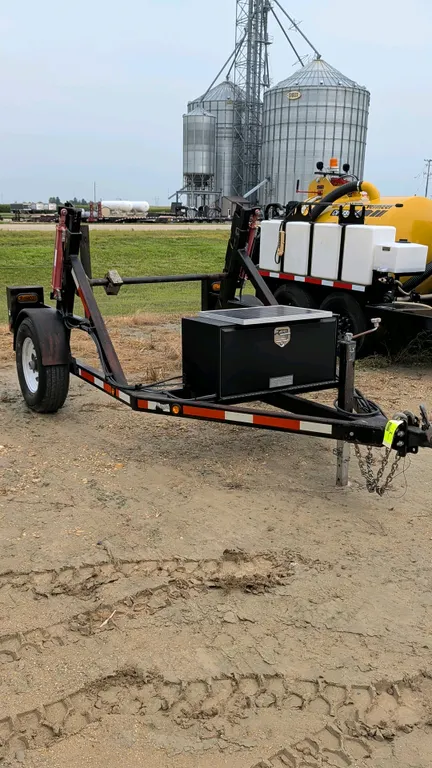 Custom hydraulic lift reel trailer. Features dual hydraulic lift cylinders, a spindle reel bar, and a tongue-mounted black toolbox with an integrated