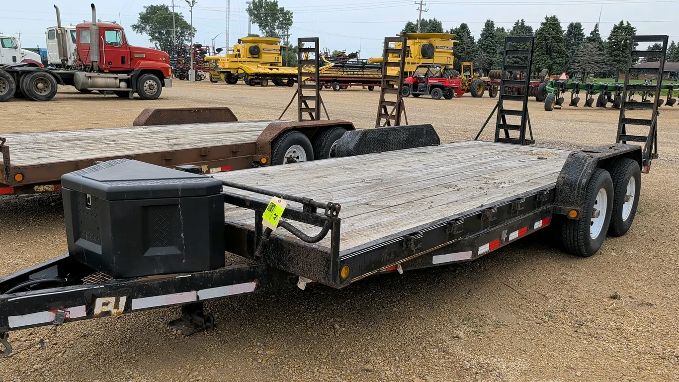 2012 PJ bumper hitch twin-axle flatbed trailer. Features a wood deck, beaver tail, (2) fold-up ladder ramps, and a tongue-mounted polymer toolbox. Dim