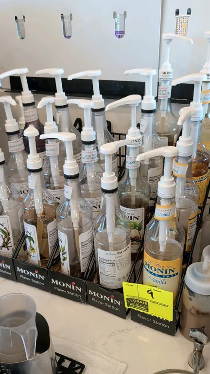 Monin Flavor Station wire syrup bottle display racks. Includes assorted Monin flavoring syrup bottles and dispensing pumps. Features multi-tier wire c