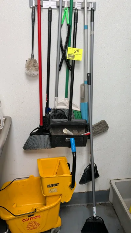 Assorted maintenance and cleaning tools. Includes Hubert yellow mop bucket with wringer on casters, Hubert upright lobby dustpan, assorted brooms, mop