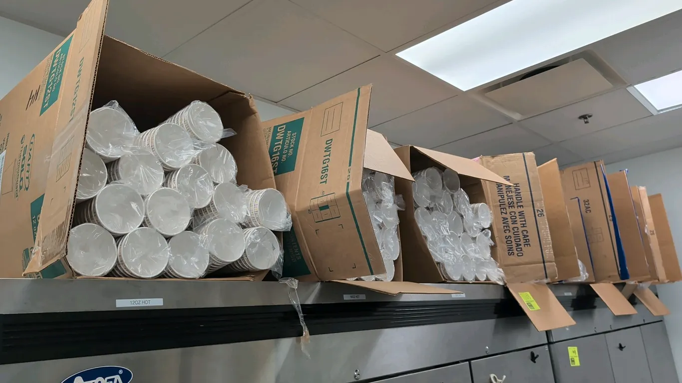 Assorted disposable drinkware supplies. Includes boxed cases of Dart Solo paper hot cups, clear plastic cold cups, and lids in various sizes including