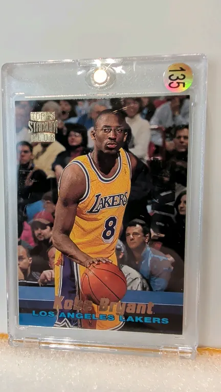 A 1996 Topps Stadium Club Kobe Bryant Rookie Card. (Topps, 1996) A Topps Stadium Club rookie trading card, #R12, featuring Kobe Bryant in his Los Ange