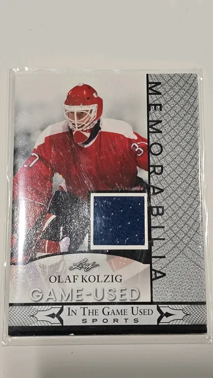 An Olaf Kolzig Game-Used Memorabilia Trading Card. (Leaf, 2024) An "In The Game Used Sports" card (Card No. GUM-106) featuring Olaf Kolzig with an emb