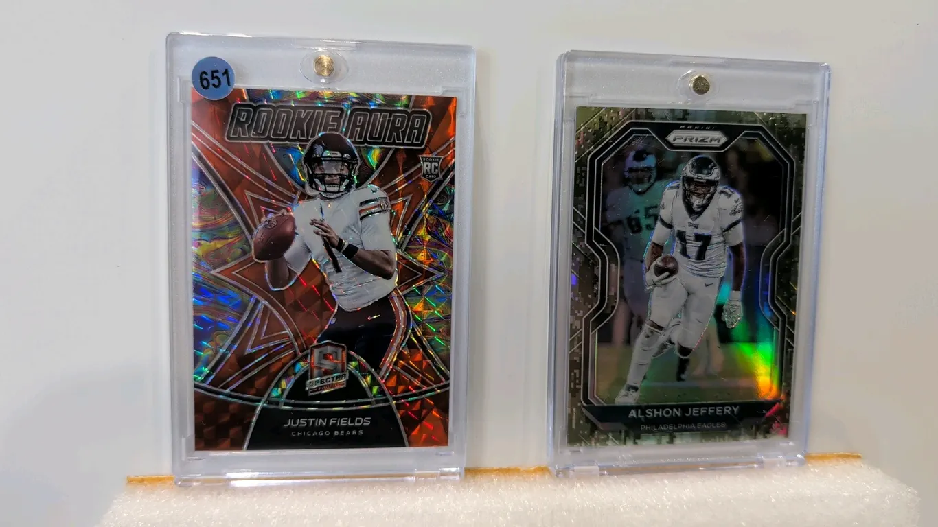 A Pair of Panini NFL Trading Cards. (Panini, 2020-2021) Includes a 2021 Spectra Justin Fields Rookie Aura No. RO-3 serialized 07/10 and a 2020 Prizm A