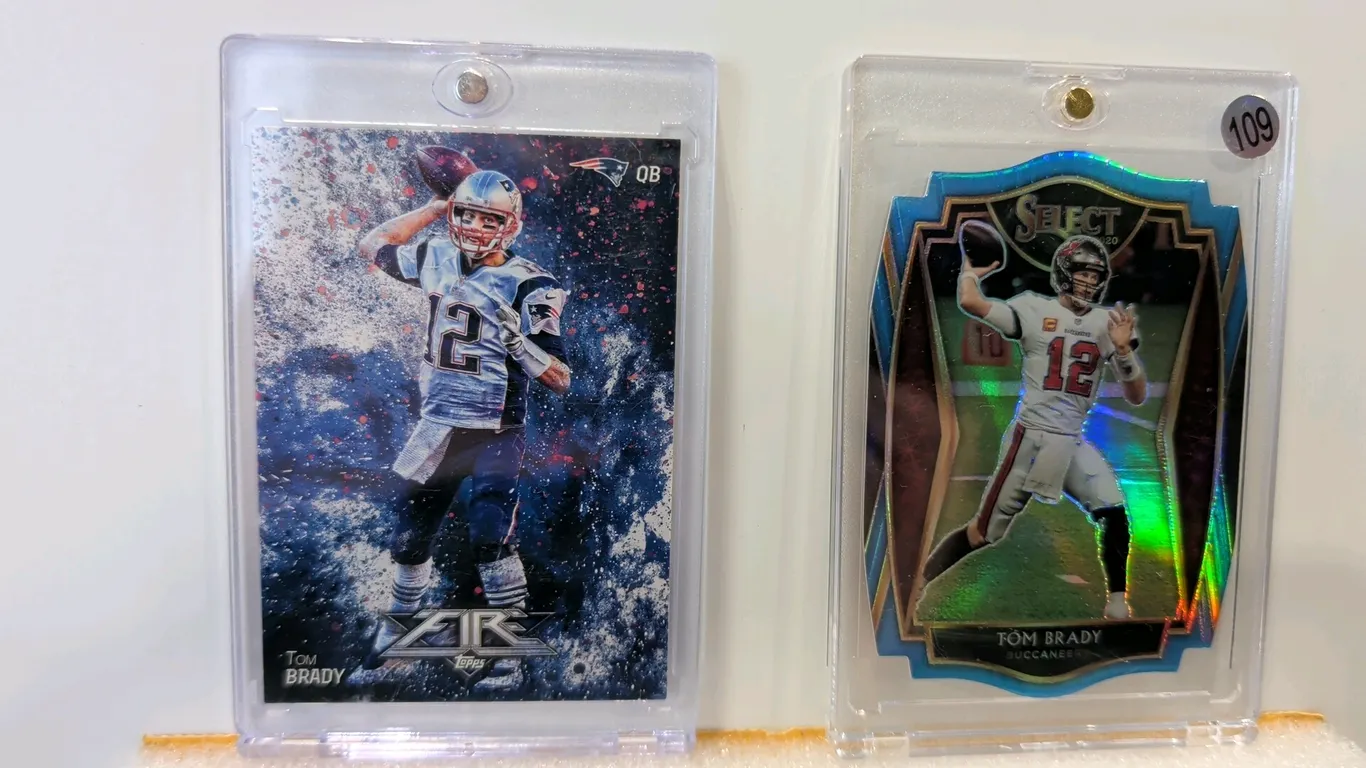 A Pair of Tom Brady NFL Trading Cards. (Topps / Panini, 2014-2020) A pair of cards featuring legendary quarterback Tom Brady. Includes a 2014 Topps Fi