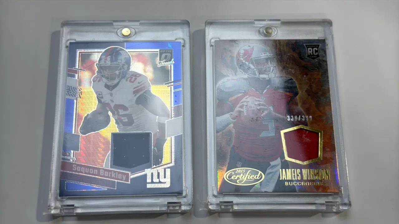A Pair of Panini Football Relic Cards. (Panini, 2015-2023) Includes a 2023 Donruss Optic Saquon Barkley Optic Threads card (No. DT-SB) with jersey swa