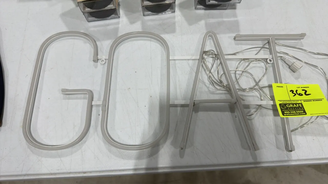 LED "GOAT" sign. Features white neon-style LED lettering mounted on a support frame. Includes power cord with a 2-pin screw-on connector. Approx. 24"