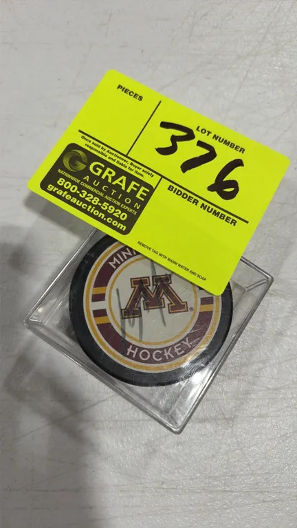 An Autographed Minnesota Gophers Hockey Puck. A hockey puck featuring the University of Minnesota Gophers logo, signed across the front face in marker