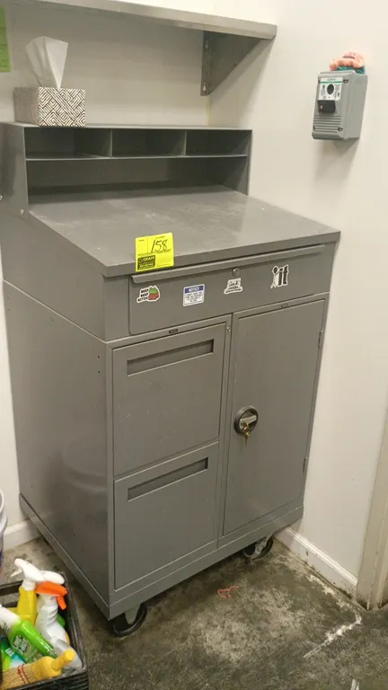 Metal portable shop desk. Features a sloped writing top, upper organizer compartments, one top drawer, two lower drawers, and a locking cabinet door w