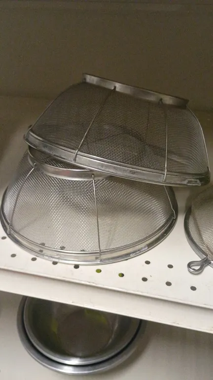 Stainless steel mesh strainers and colanders. Includes (2) footed wire mesh colanders and (1) handled wire mesh strainer with dual pan rests and green